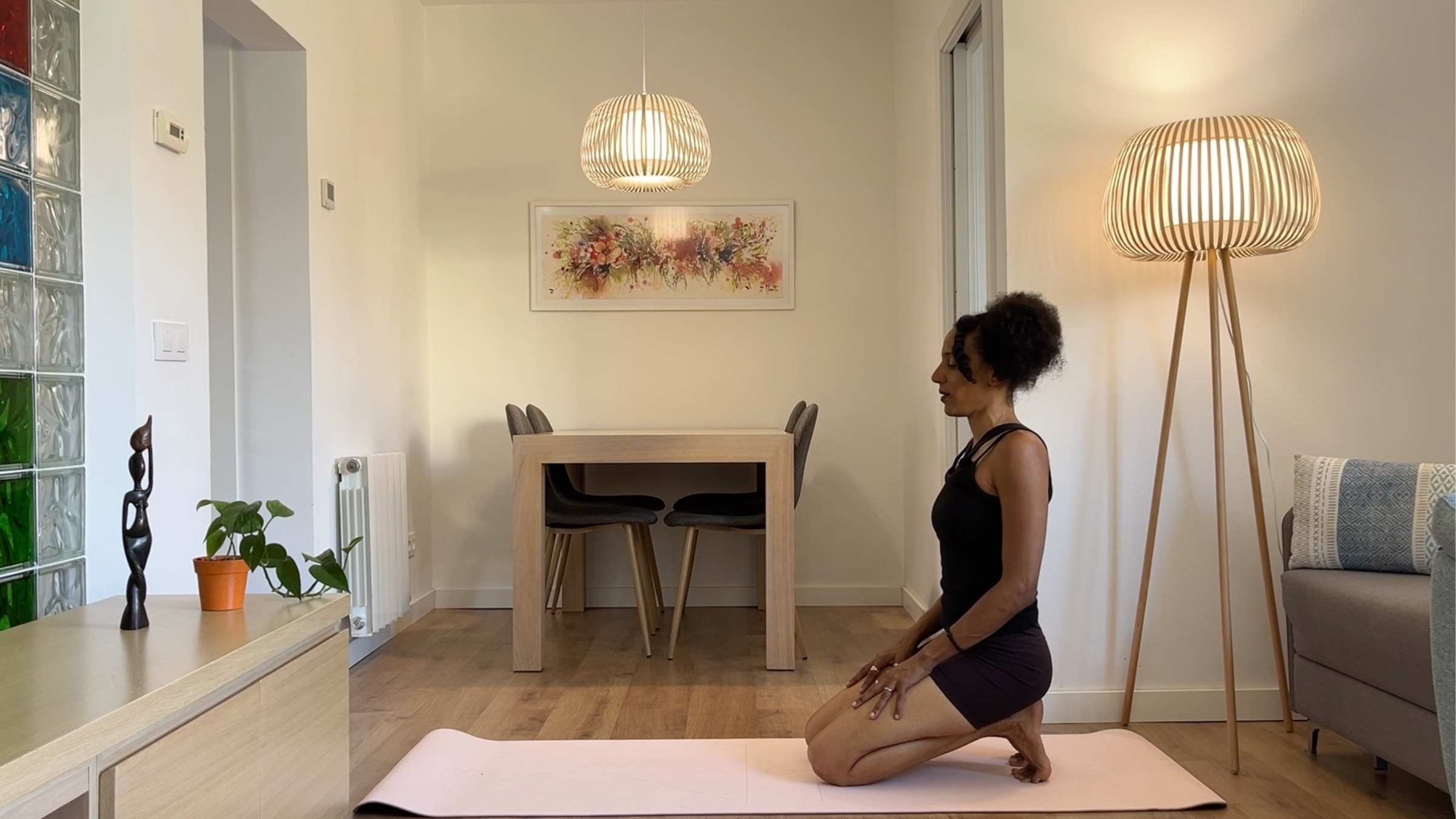 A person kneeling on a yoga mat with their toes tucked under, sitting back on their heels with an upright posture and hands resting gently on their thighs.